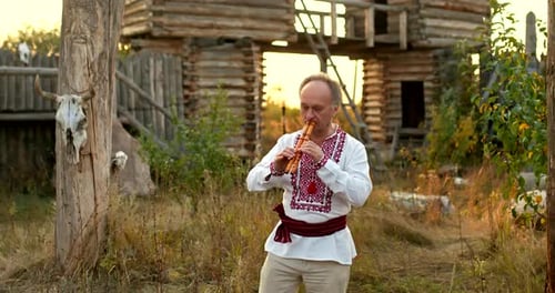 Mann in einem slawisch-ukrainischen Volkskostüm spielt eine Doppelpfeife in einem Dorfhof