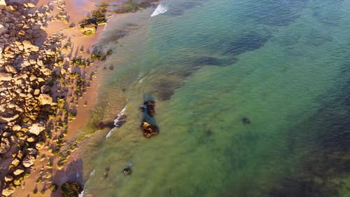 Amazing scenic drone aerial view of the beach and ocean with calm waves during a sunset.