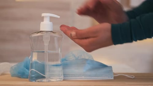 Hands Using Hand Sanitizer Next to Mask