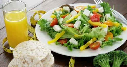 Vegetable salad with glass of juice, granola bar and measurement tape
