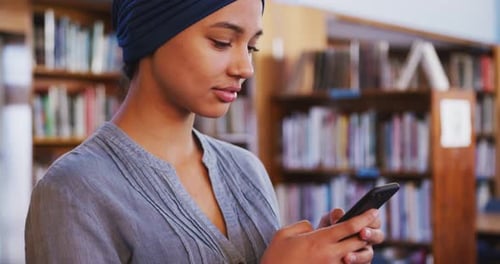 Student Using Smartphone in Library Bookshelves
