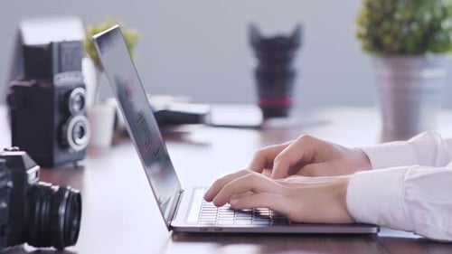 Hands Typing on Laptop with Cameras on Desk