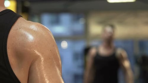 Hombre musculoso levantando pesas grandes frente al espejo, entrenamiento activo en el gimnasio