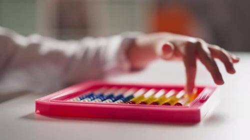 Una niña cuenta a mano pequeñas cuentas en movimiento en un ábaco de juguete