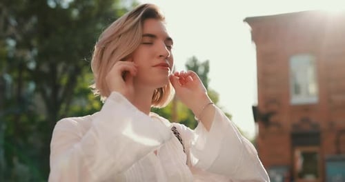 Woman Puts on Wireless Earbuds in a Summer City Slow Motion
