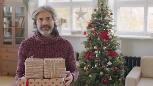 Man Holding Christmas Gifts Near Decorated Tree Indoors