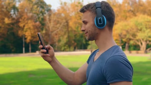 Young Man Using Phone with Headphones in Park