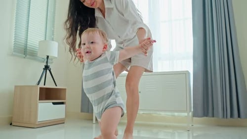 Caucasian baby boy child learn to walk, taking first step on floor with parents support in house.
