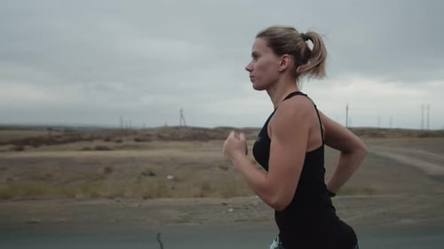 Woman of Athletic Build in Sportswear is Jogging Outdoors Side View