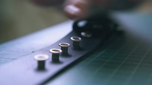 Craftsperson adds Metal Eyelets to Leather Strap