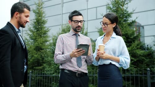 Men and Woman Discussing Work Near Office Building Looking at Tablet Screen