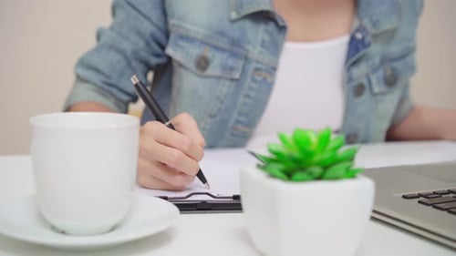 Asian young woman owner of SME checking product on stock and write on clipboard working at home.