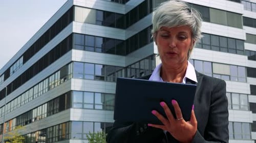 Business Middle Age Woman Works on the Tablet - Company Building in the Background