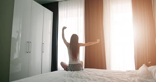 Young Woman Stretching on Bed in Morning Sunlight