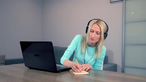 Woman Works at Home on Laptop with Headphones or Headset