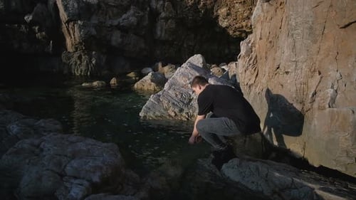 Young man in a black T-shirt is resting in a tent on the rocks by the sea