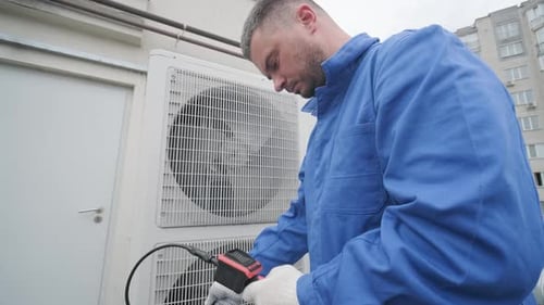 Man Repairs Air Conditioning Unit on Building Exterior