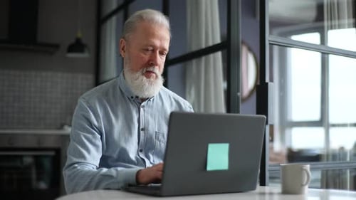 Senior Man Works On Laptop At Home