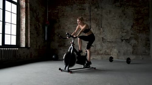 Young active woman spinning air bike in gym. Female training on air bike in slow motion