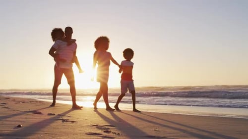 African american family having fun walking together during sunset on the beach