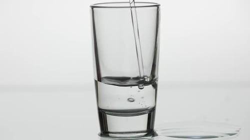 Pouring Up Shot of Vodka Into Drinking Glass. Slow Motion. White Background