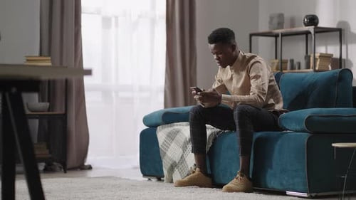 Young Man Relaxing on Couch Using Mobile Phone