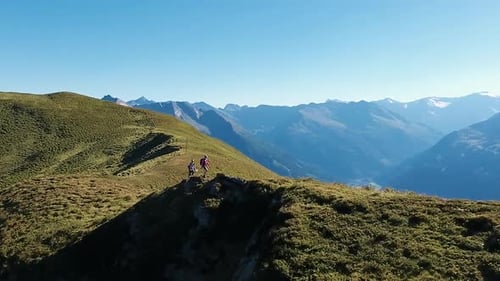 Zoomed in aerial drone shot of a couple walking along an Alpine mountain ridge with a stunning mount