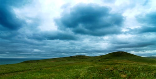 Green Hills and Grassland Near Ocean Under Cloudy Sky