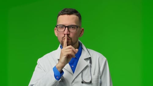 Hübscher junger Mann mit Bären in Arztuniform bittet darum, mit dem Finger auf den Lippen still zu sein