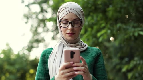 Muslim Businesswoman with Smart Phone in Hijab Walking in Summer Park