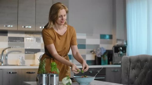 Woman Making Salad With Fresh Basil in Kitchen