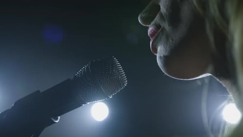 Close-up of the Face of the Singer with Microphone on a Black Smoky Background. The Singer Sings a