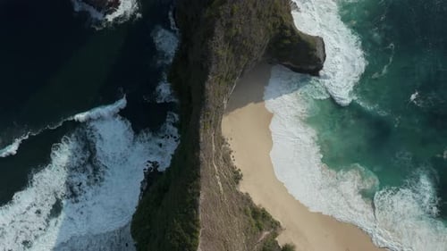 Top down aerial view of a small beach and towering cliffs