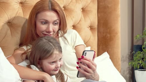 Woman and Girl Looking at Smartphone in Bed