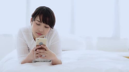 Young Woman Relaxes in Bed with Smartphone