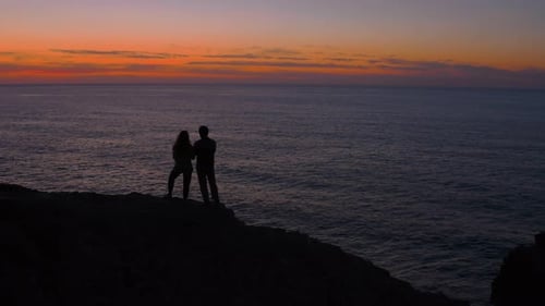 Silhouette of Couple Walk on Cliff Edge at Sunset