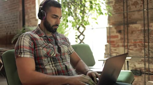 Man with Headphones Uses Laptop in Modern Workspace