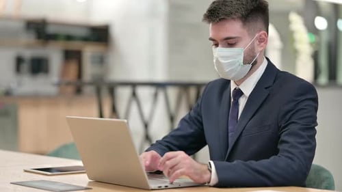 Man Wearing Mask Working on Laptop in Office