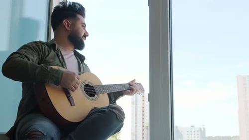 Young Man Plays Guitar by Apartment Window