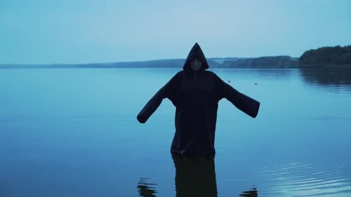 Mysterious Hooded Figure Standing in Water at Night