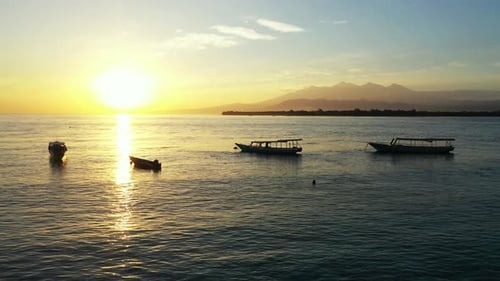 Tranquil bay with anchored boats near shore of tropical island at sunset yellow sky reflecting over