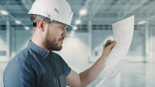 A Man Worker is Holding Construction Blueprint and Making Notes at Building Site