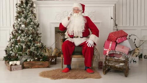 Jolly Santa Claus Sitting By the Christmas Tree and Talking on the Phone