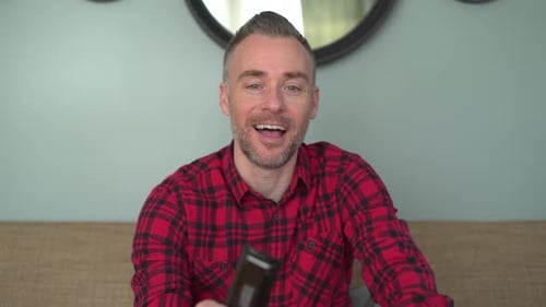 Man Holding Remote Laughing on Couch Indoors