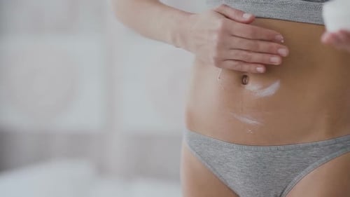 Frau trägt Feuchtigkeitscreme auf ihren Bauch auf