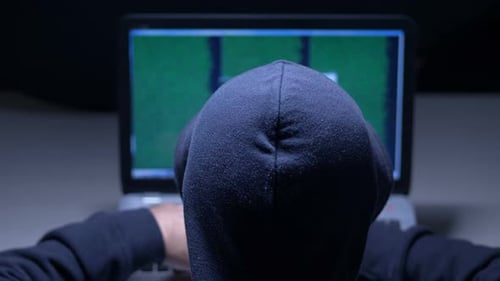 Hacker in Hood Cracking Code Using Laptop in A Room