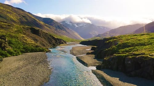 Flying Above a Glacial River in Iceland with Snowy Mountains in the Background
