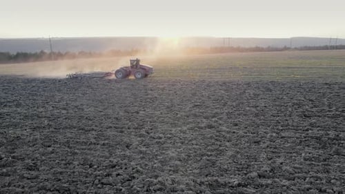 Drone Tracking Shot of Farming Tractor Plowing Dry Field After Collecting Harvest Pillar of Dust