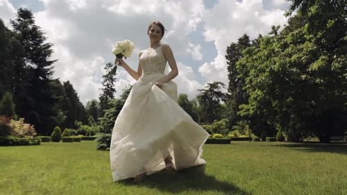 Beautiful Stylish Bride in White Wedding Dress and Veil Holding Wedding Bouquet in Hands in Park