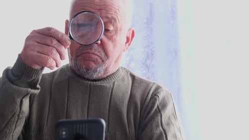 Senior Man Reads Mobile Phone with Magnifying Glass
